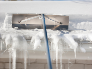 Roofing professional safely removing snow from a roof in Rehoboth Beach to prevent ice dams.