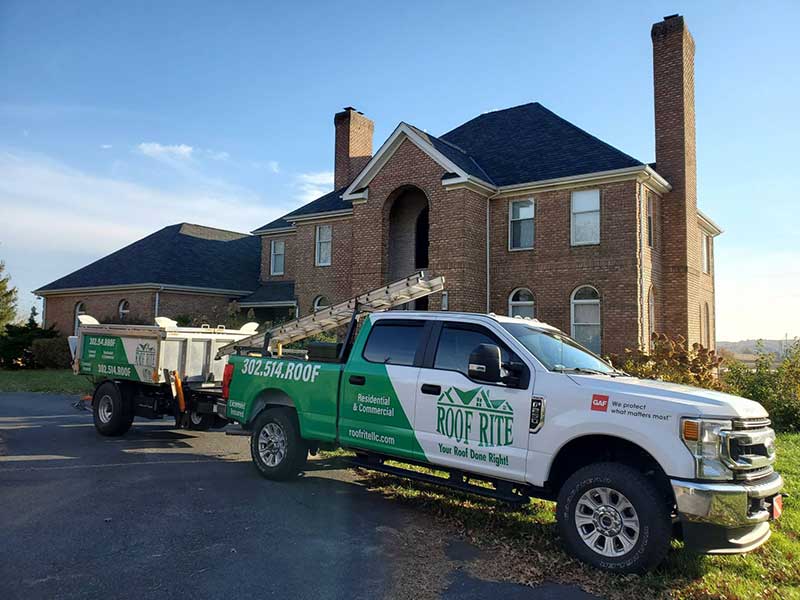 Roof Rite work pickup and Equipter parked in front of a large brick home