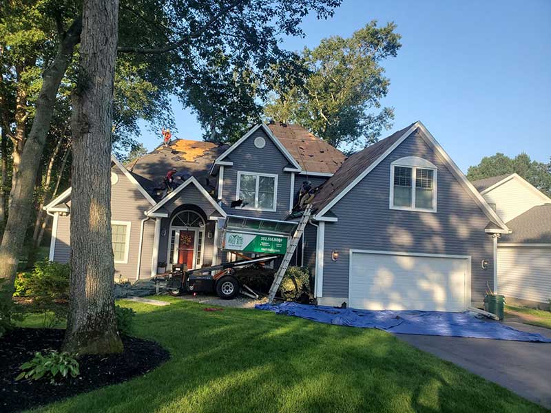 Roof Rite crew tearing off old shingles on a residential roof with their Equipter parked nearby in New Castle County
