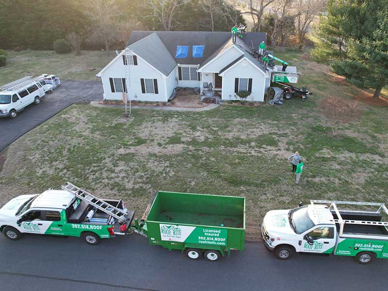 Roof Rite crew finishing up a shingle installation on a residential roof with their work trucks parked in front and an Equipter to the side